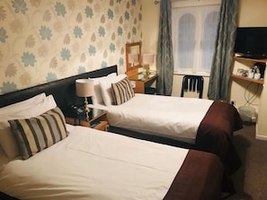 A hotel room with two beds, a desk with a lamp, a television, and a window with curtains. - Dobbins Inn (Carrickfergus)