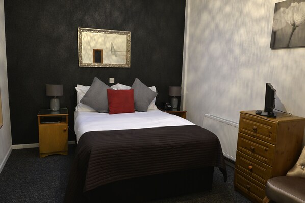 A bedroom with a bed, two bedside tables, a dresser, a mirror, and a radiator.