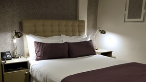 A neatly made bed with a tufted headboard, two bedside lamps, a nightstand with a phone, and a framed picture on the wall. - Dobbins Inn (Carrickfergus)