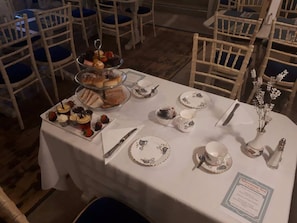 A table set for a tea service with a menu, tea cups, saucers, and a tiered dessert display. - Dobbins Inn (Carrickfergus)