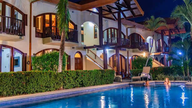 Un hotel de varios pisos con piscina, balcones y palmeras.