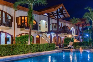 Un hotel de varios pisos con piscina, balcones y palmeras.