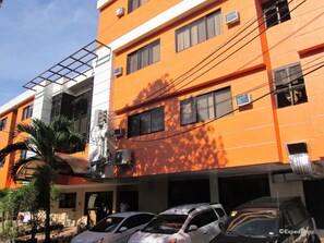 A multi-story building with a bright orange facade, air conditioning units, and a parking garage below.