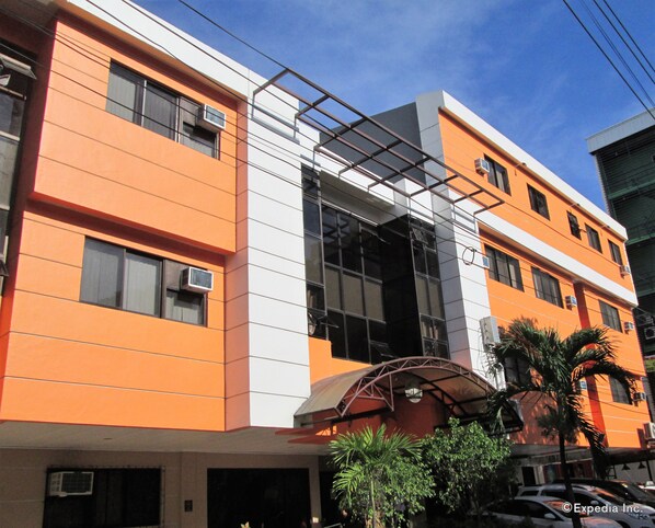 A modern building with orange and white exterior walls, large windows, and a covered entrance area with palm trees.