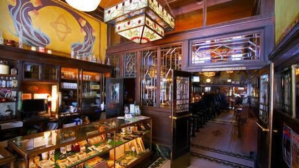 A bar with a glass display case of snacks, a mural on the wall, and a staircase leading to an upper level. - McMenamins Olympic Club (Centralia)