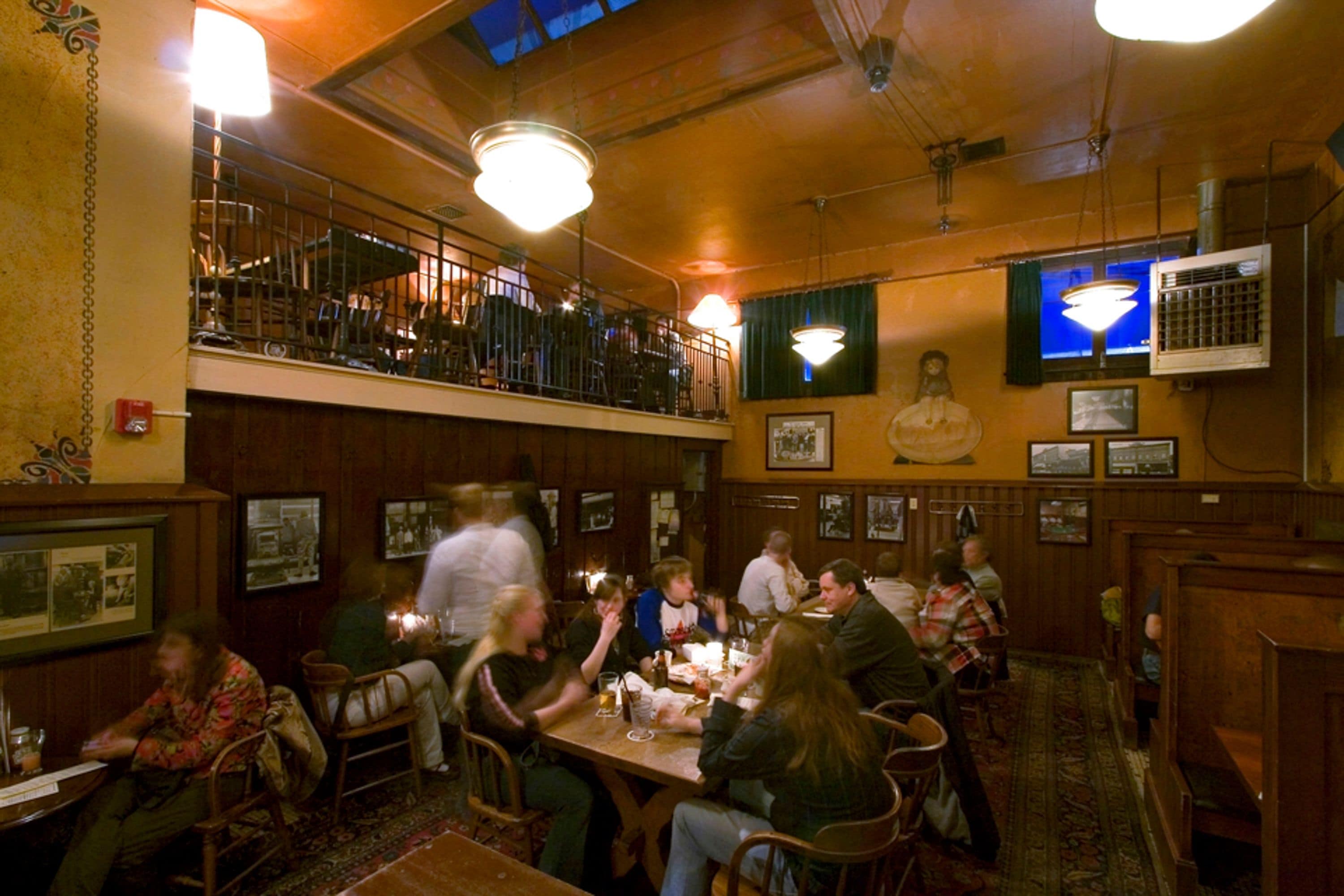 A restaurant with wooden interiors, a balcony, and a large TV screen.