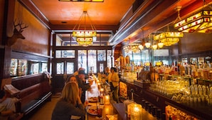 A bar with wooden benches, a bartender, and a well-stocked liquor shelf. - McMenamins Olympic Club (Centralia)