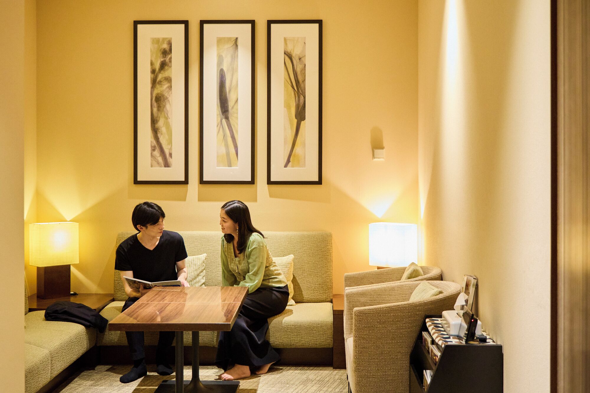 A hotel room with a sofa, a small wooden table, and three framed abstract paintings on the wall.