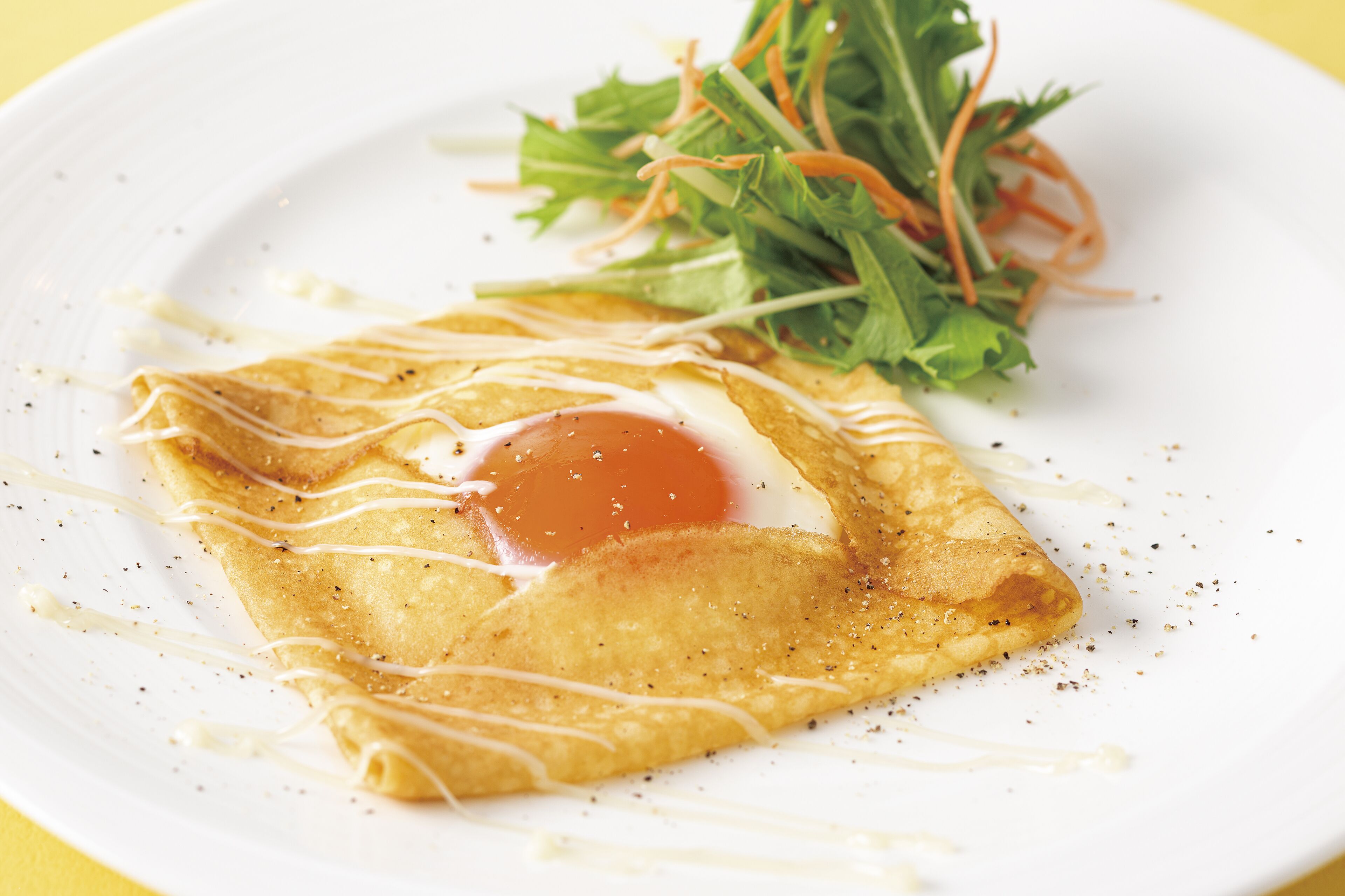 A folded crepe with a poached egg and a side salad on a white plate.