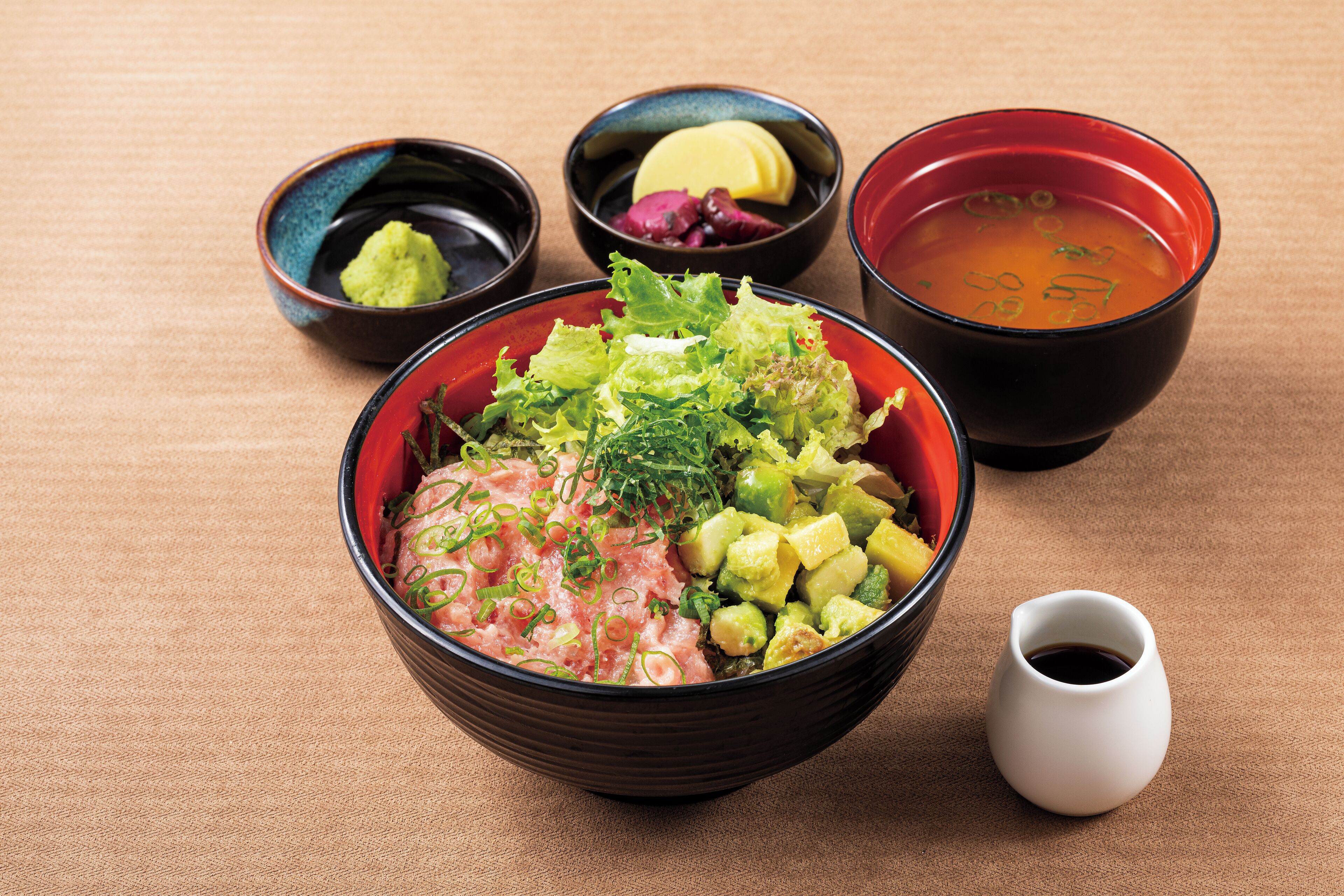 Un bol de sashimi con aguacate y cebolletas, acompañado de pequeños recipientes de wasabi, jengibre encurtido y salsa de soja.