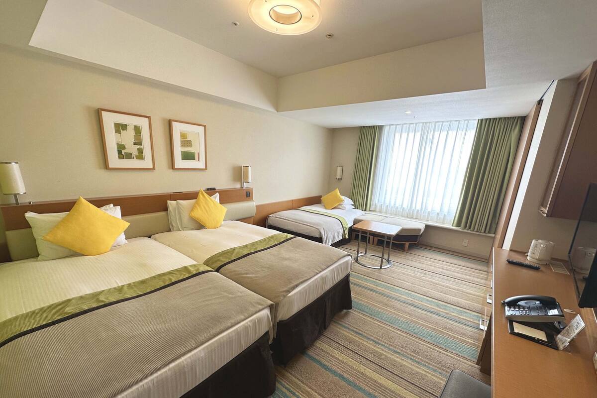 A hotel room with two beds, a small table, a desk with a phone, and a TV.