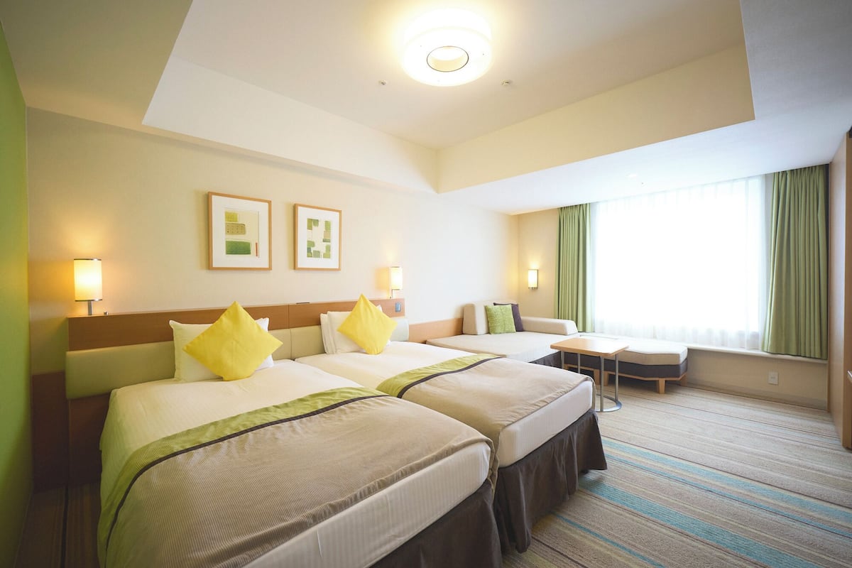 A hotel room with two beds, a small table, and a window with curtains.