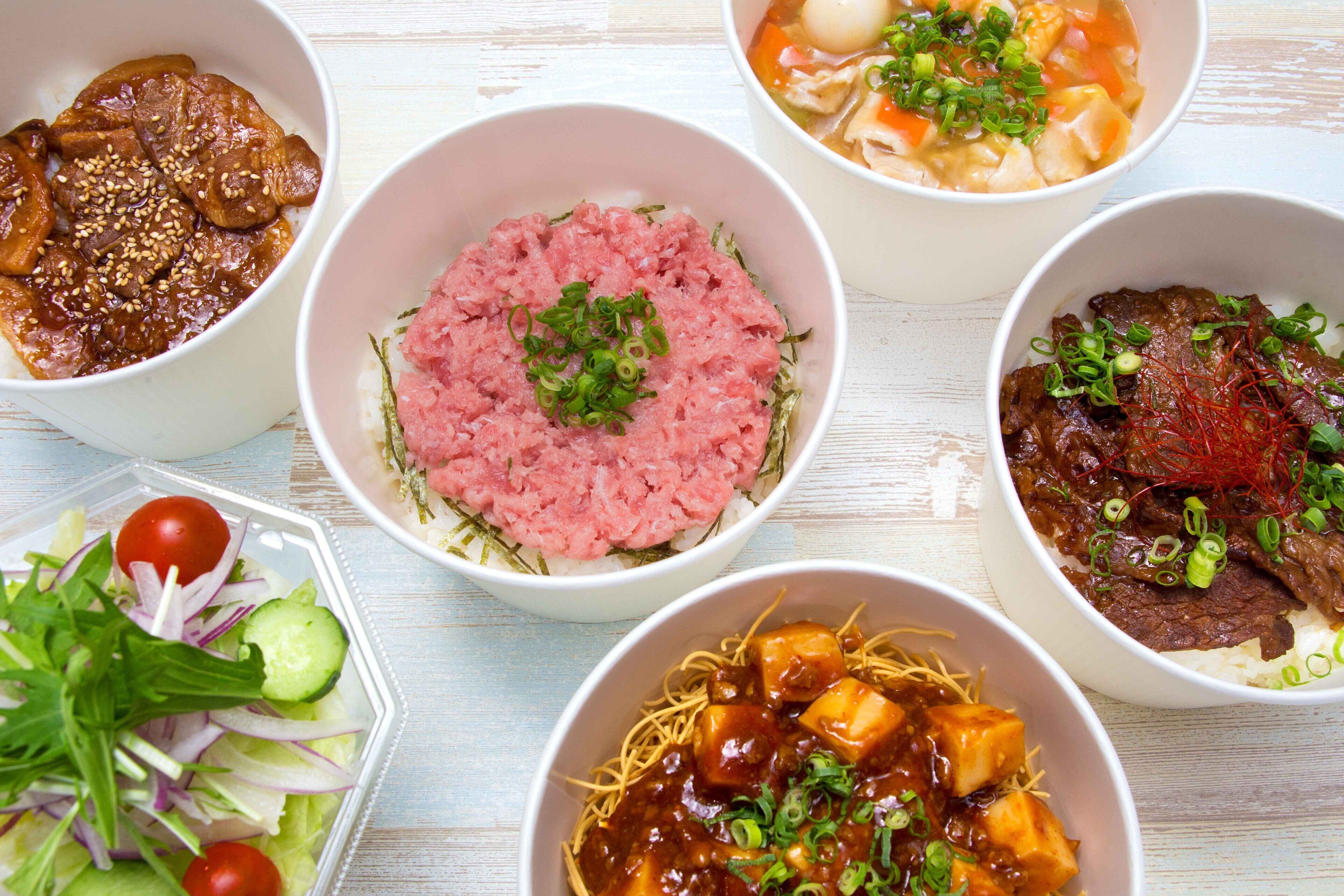 A variety of bowls containing different dishes, including rice, noodles, and meat, arranged on a table.