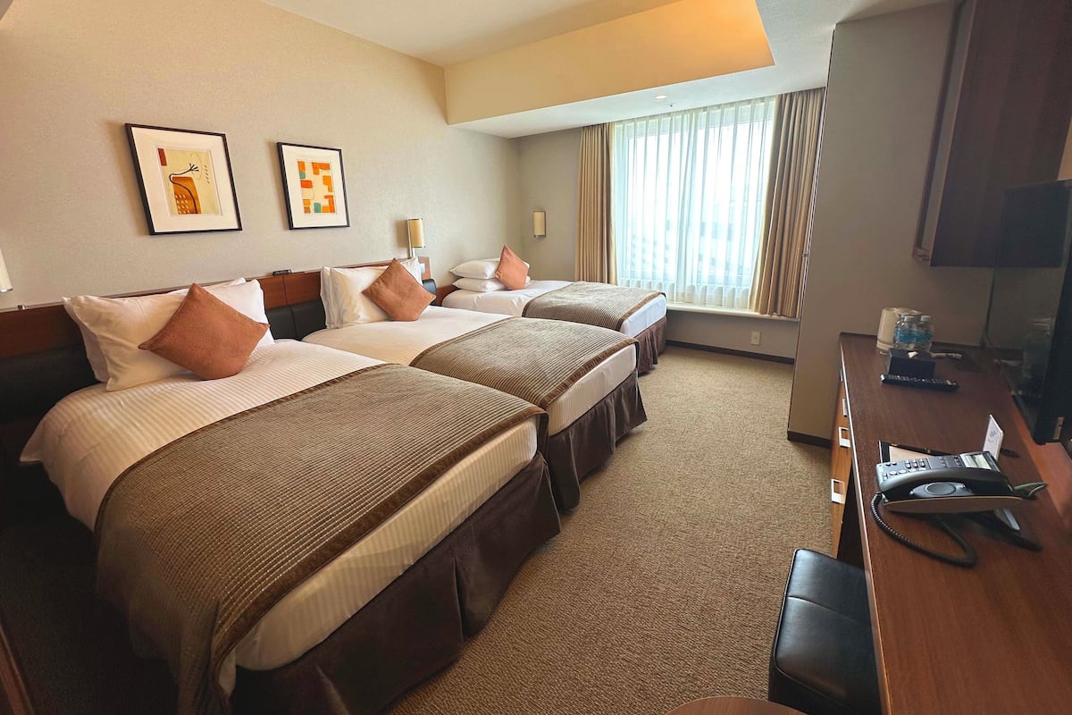 A hotel room with two beds, a desk with a telephone, and a television.