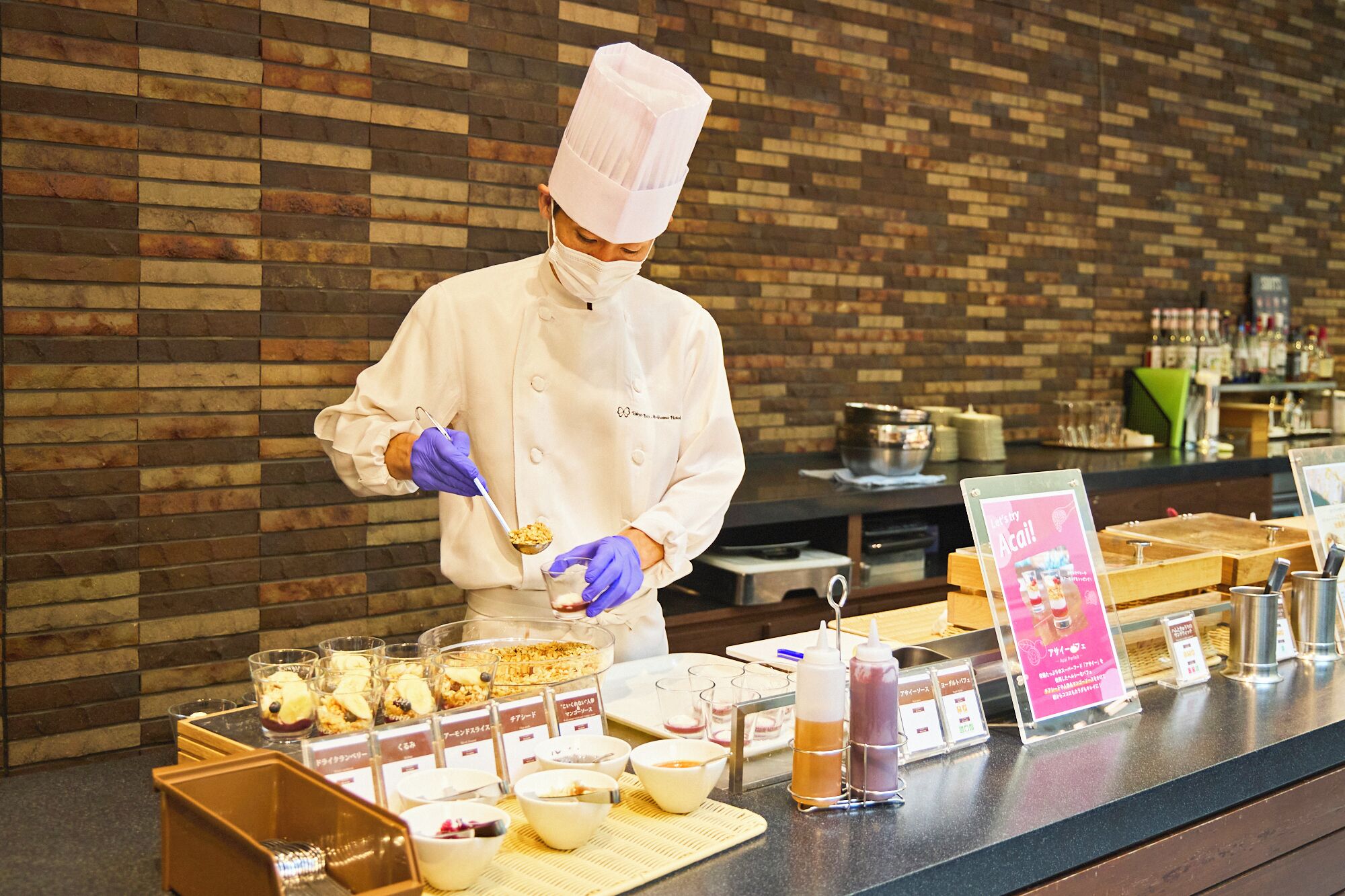 Un chef, vêtu d’une blouse et d’un chapeau blancs, prépare des plats devant un comptoir où sont disposés divers mets et condiments.