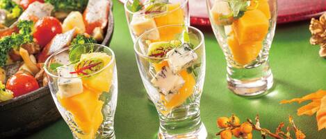 Three glasses of a fruit-based drink with garnishes, a bowl of mixed vegetables, and some decorative elements on a green surface.