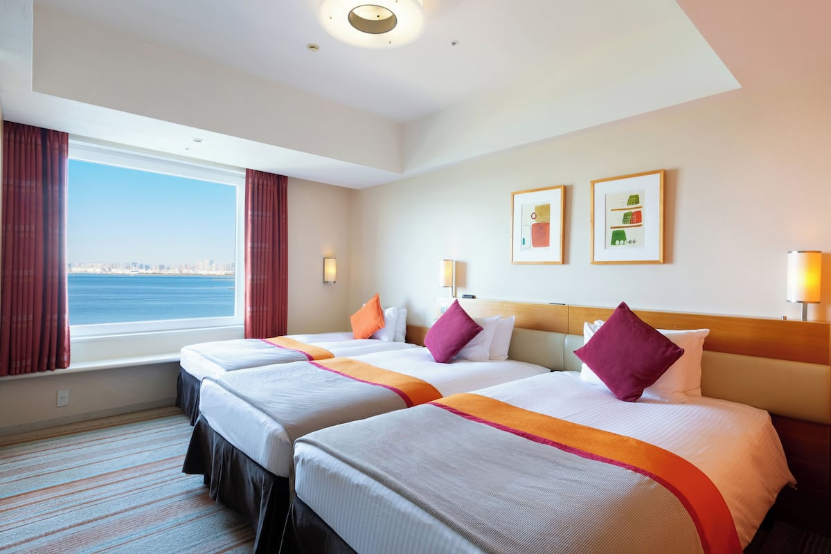 A hotel room with two beds, a large window with a city view, and two framed pictures on the wall.