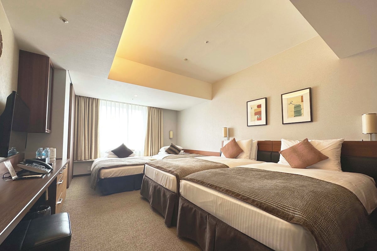 A hotel room with two beds, a desk, and a TV.