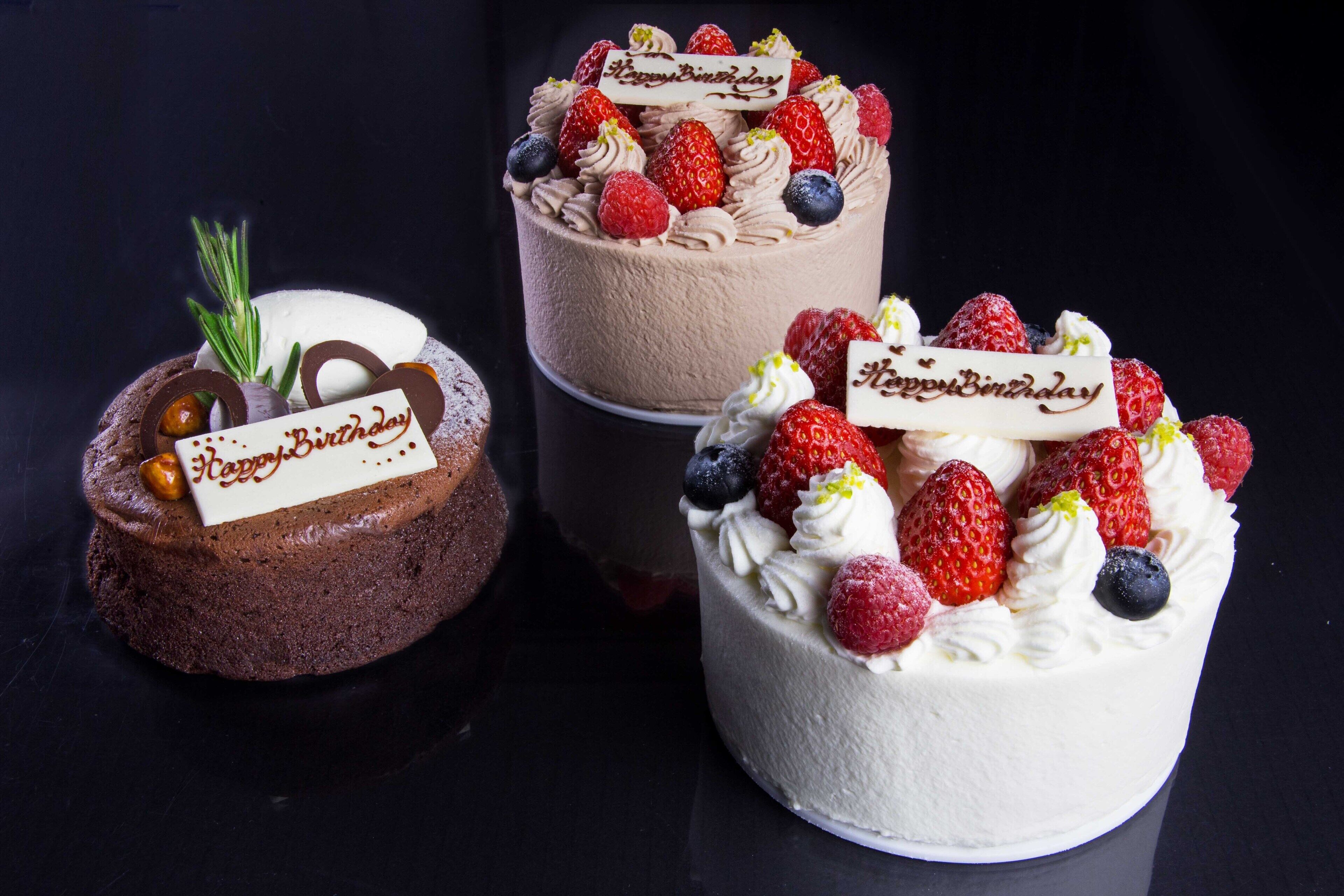 Three cakes with 'Happy Birthday' decorations and various fruits.