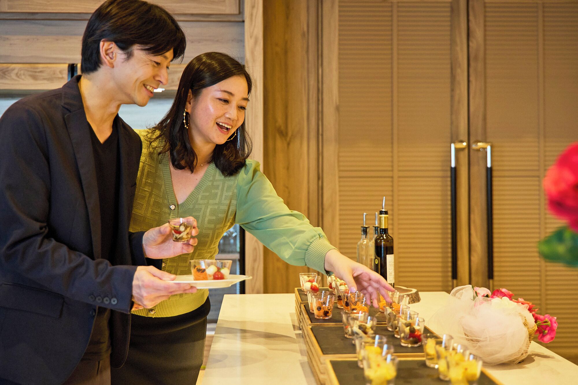 A couple standing by a table with a variety of small dishes and bottles, likely a tasting or buffet setup.