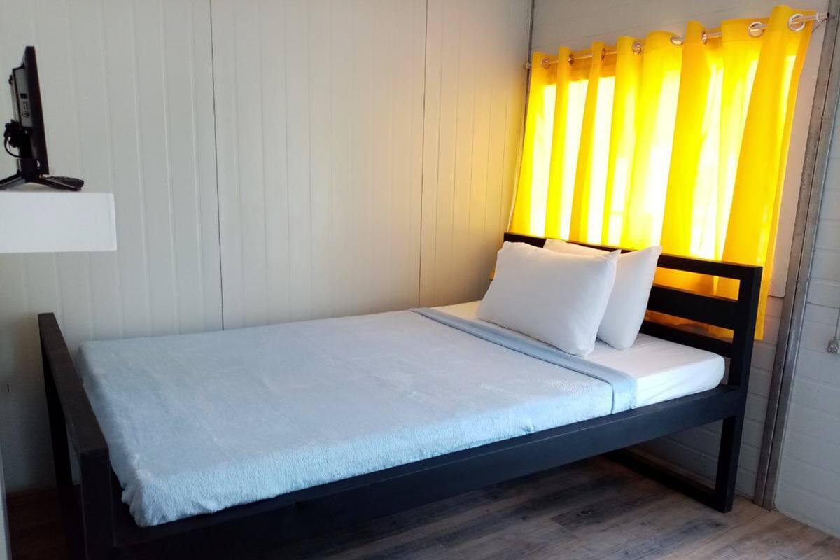 A single bed with a dark frame, white bedding, and a yellow curtain.