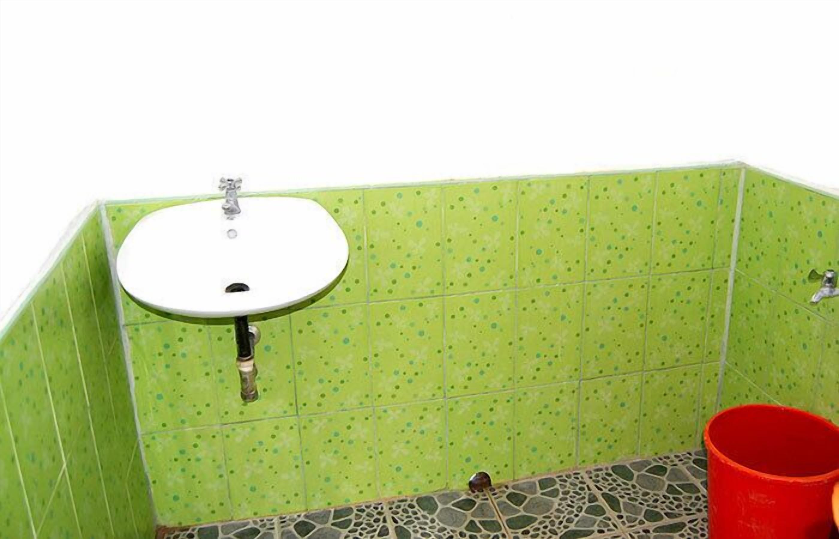 A bathroom with a green tiled wall, a white sink, and a red bucket.