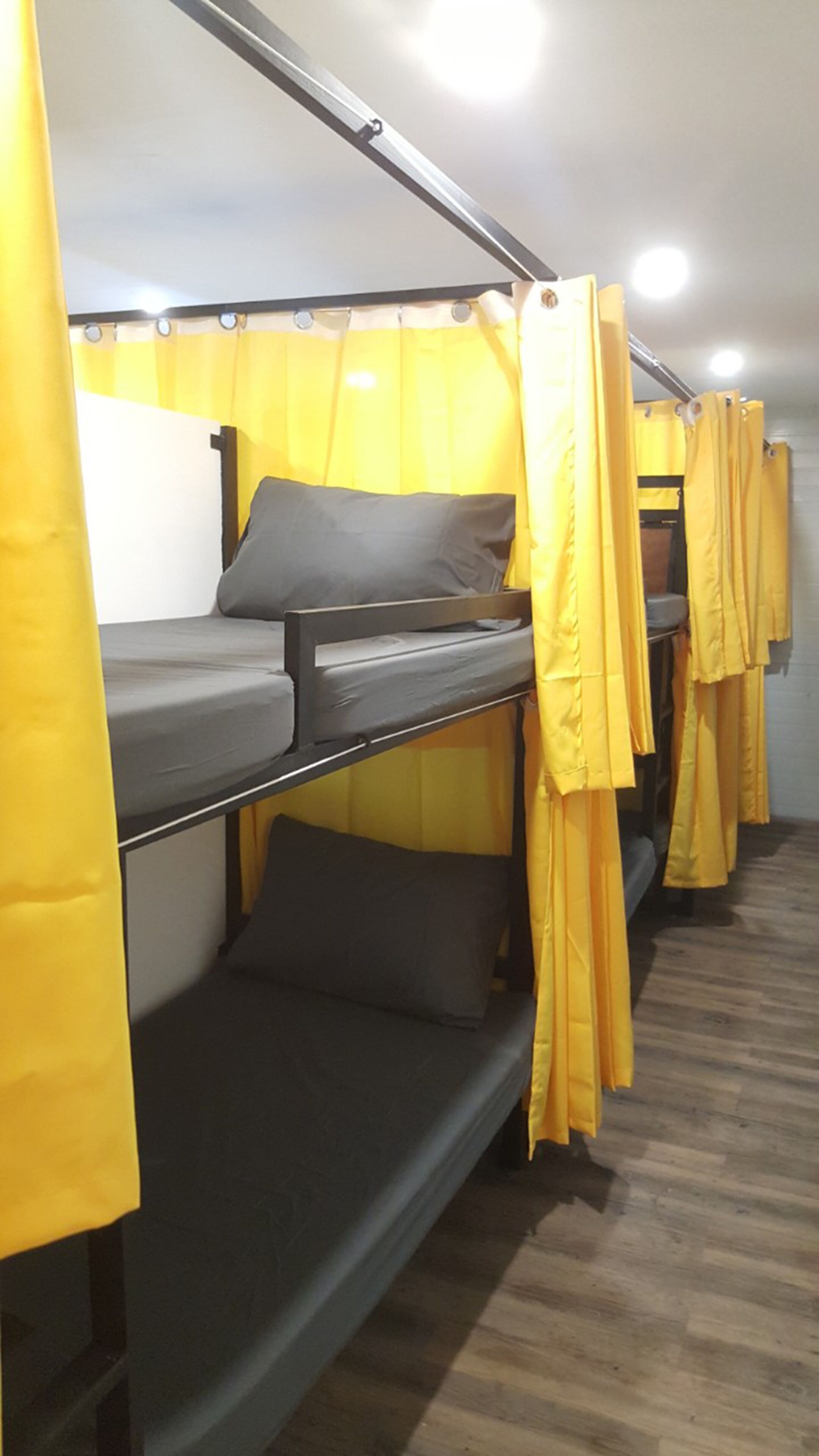 Una fila de literas con cortinas amarillas, suelo de madera y pared blanca.