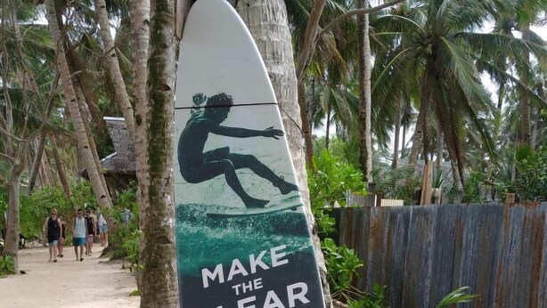 Schild am Strand mit der Silhouette einer surfenden Person, das für Sauberkeit in der Umwelt wirbt.