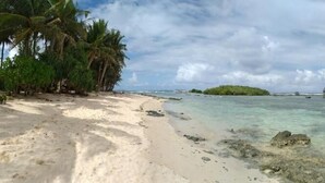 Ein Strand mit klarem türkisblauem Wasser, einem sandigen Ufer und einem Holzsteg mit Überwasservillen.