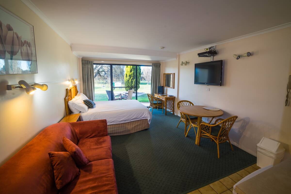 A hotel room with a bed, a sofa, a dining table with chairs, a television, and a window with a view of the outdoors.