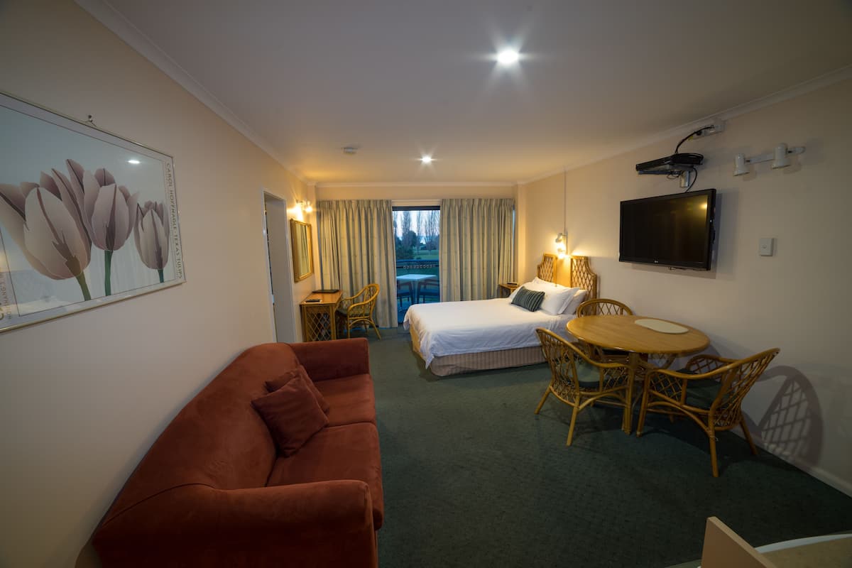 A hotel room with a bed, a sofa, a dining table, and a TV.