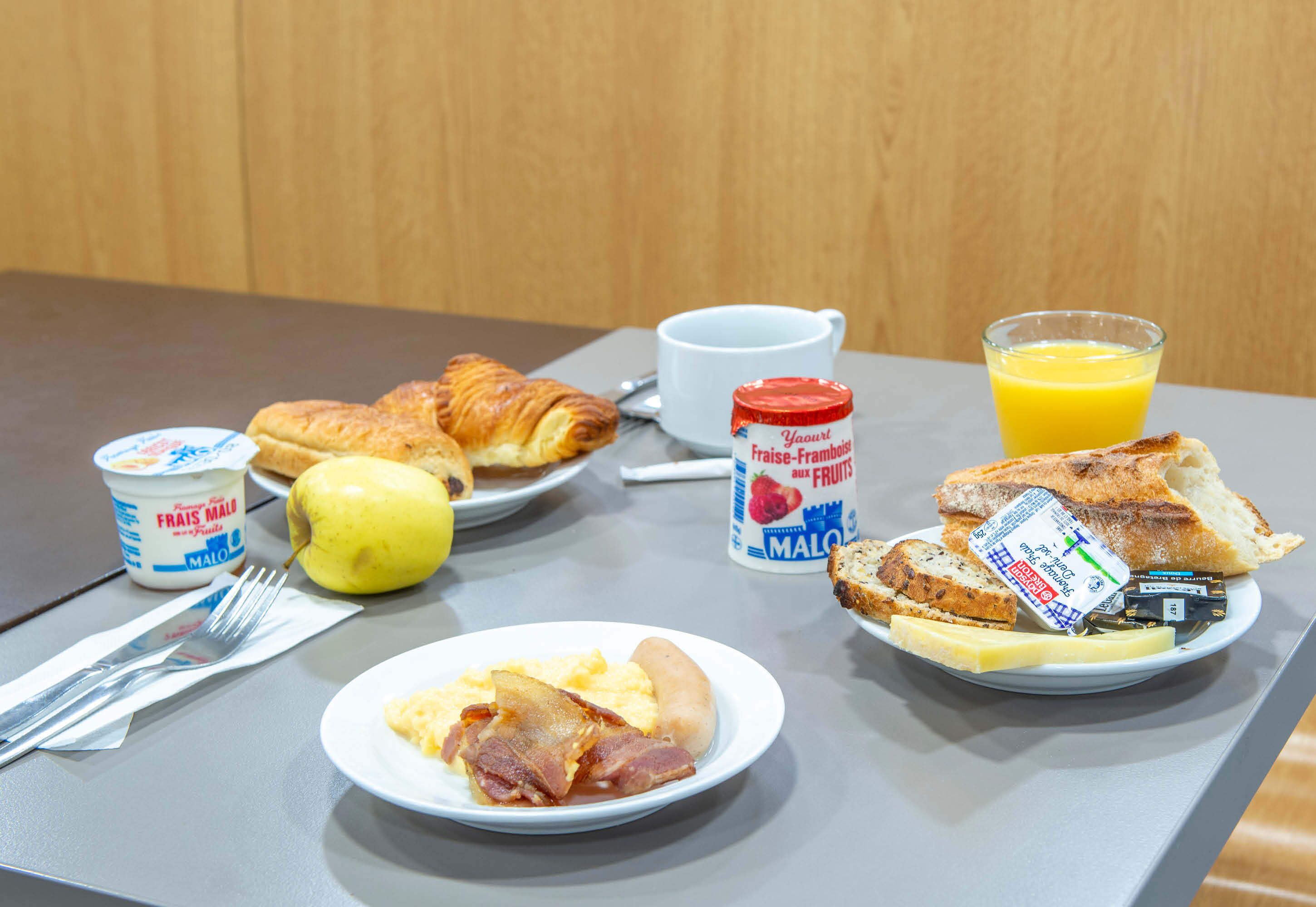 A breakfast table with croissants, fruit, yogurt, toast, and juice.