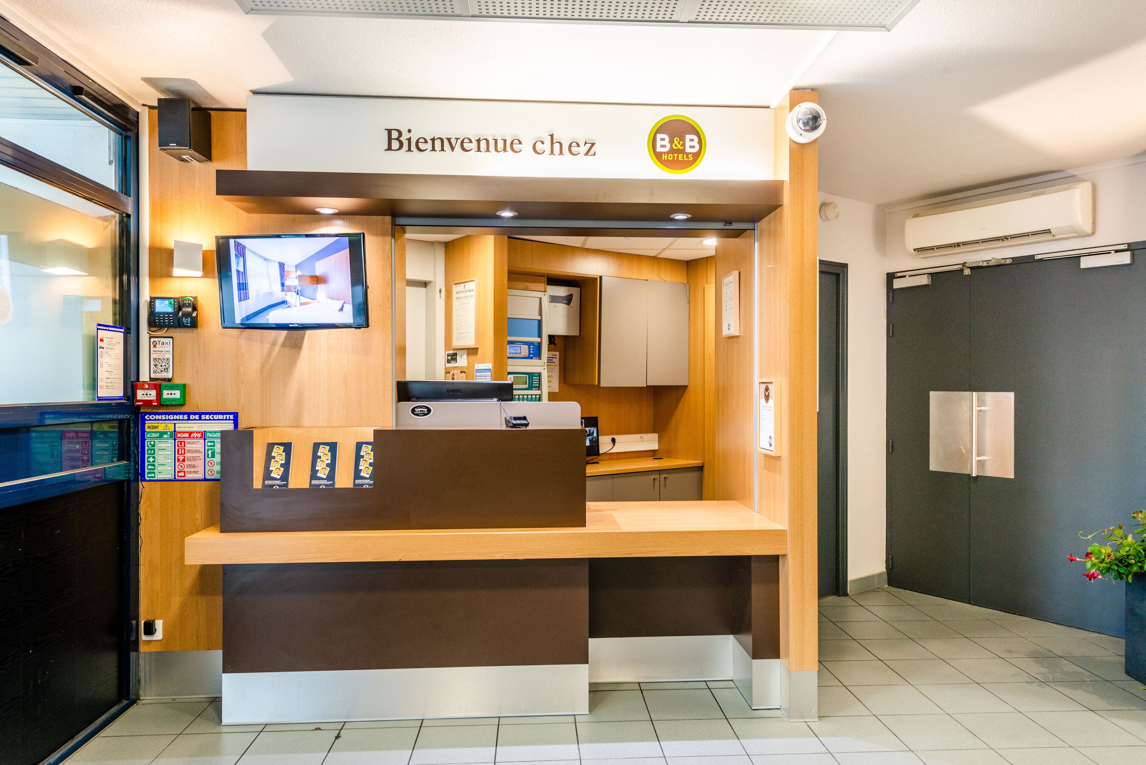 Un mostrador de recepción con una pantalla digital, una encimera de madera y un cartel que dice 'Bienvenue chez B&B Hotels'.