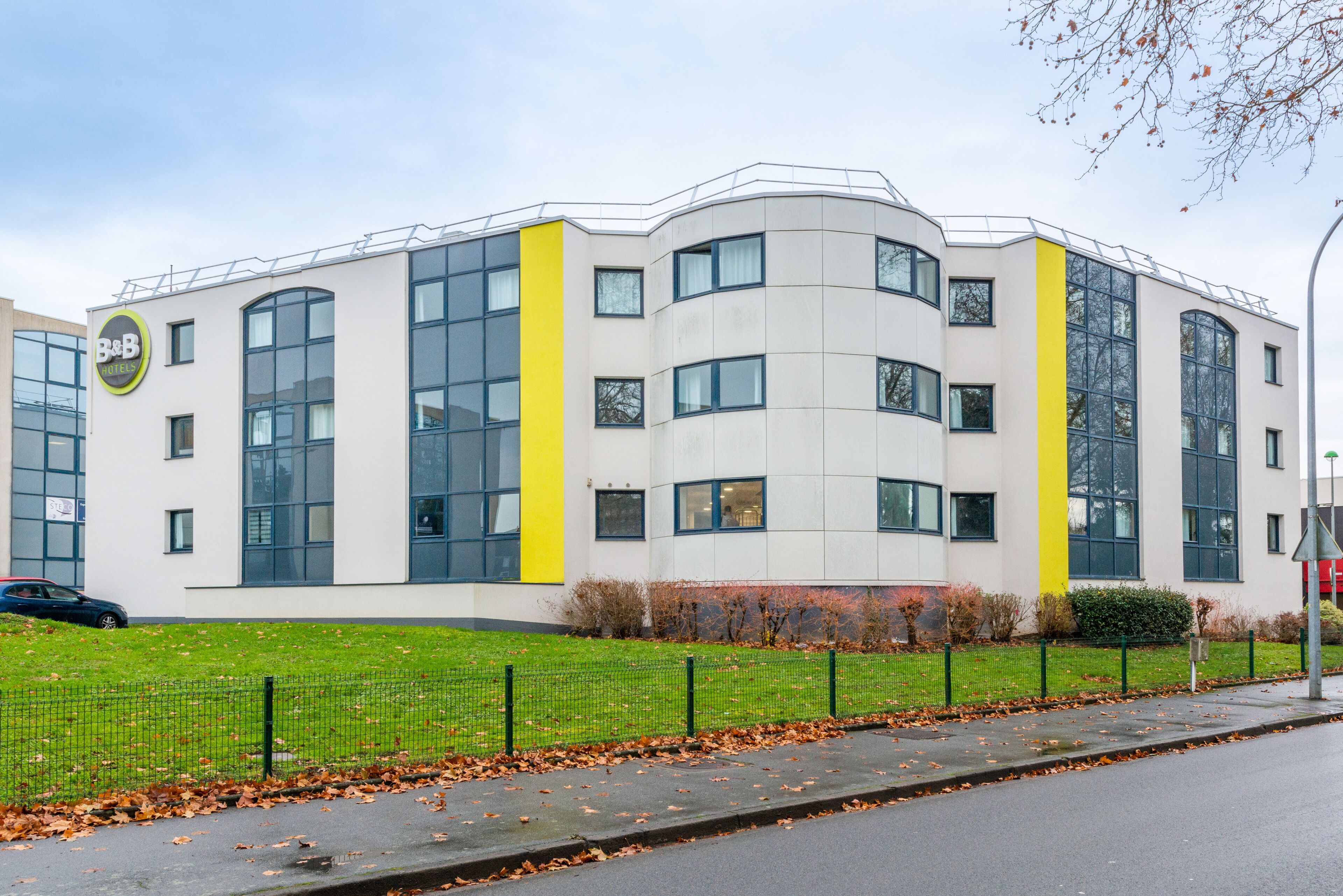 A modern B&B hotel with a curved facade, large windows, and a yellow accent wall.