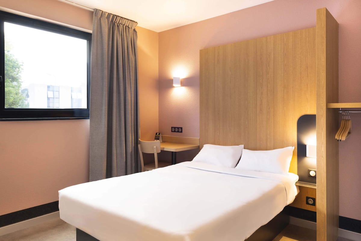 A hotel room with a large bed, a desk, and a chair.