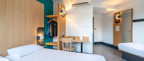 Habitación de hotel con dos camas, un escritorio, una silla, un armario y un aire acondicionado.