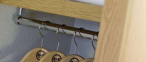 A hotel room with a neatly made bed, a towel, and wooden hangers with the hotel logo.