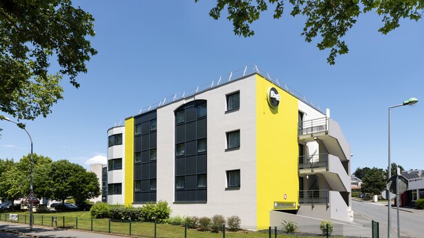 A modern building with a yellow and grey facade, large windows, and a visible entrance. - B&B HOTEL Cholet Sud (Cholet)