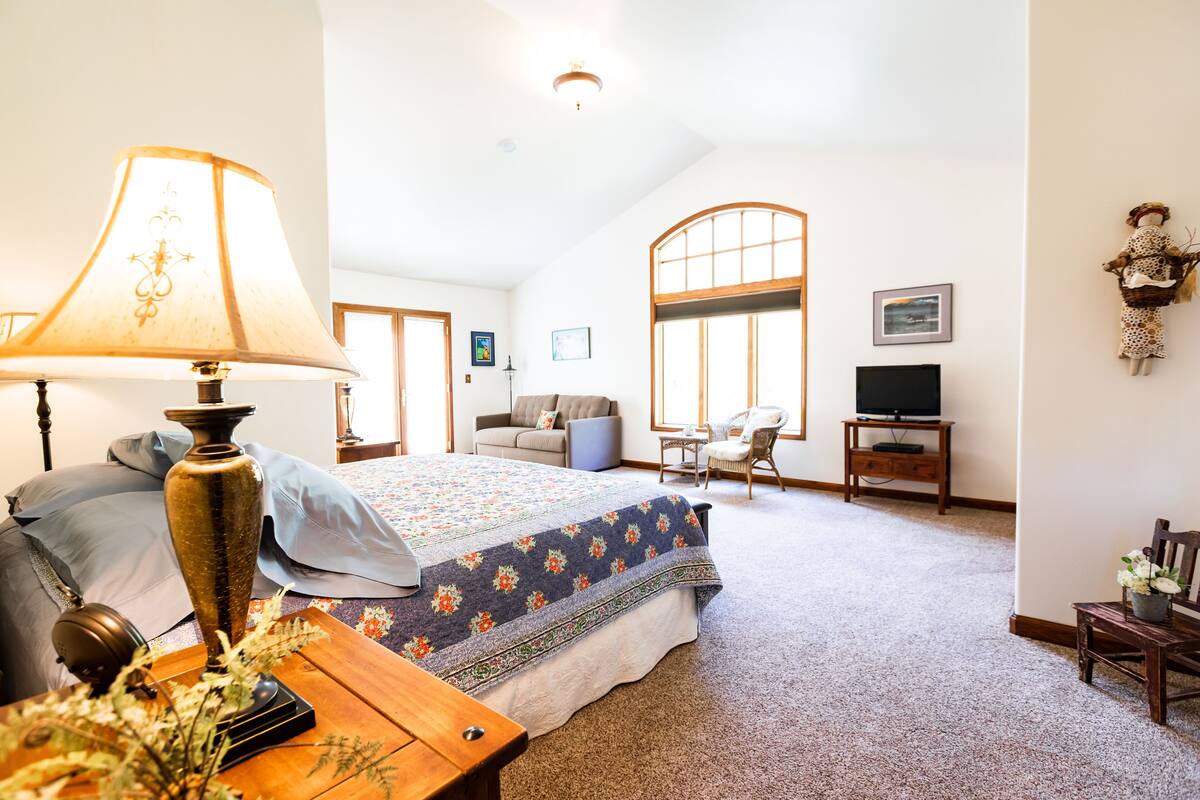 A spacious bedroom with a large bed, a sitting area with a sofa and chairs, a television, and a decorative lamp.