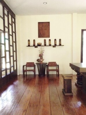 Una habitación con piso de madera, una mesa con sillas, un jarrón decorativo y varios objetos enmarcados en una estantería.