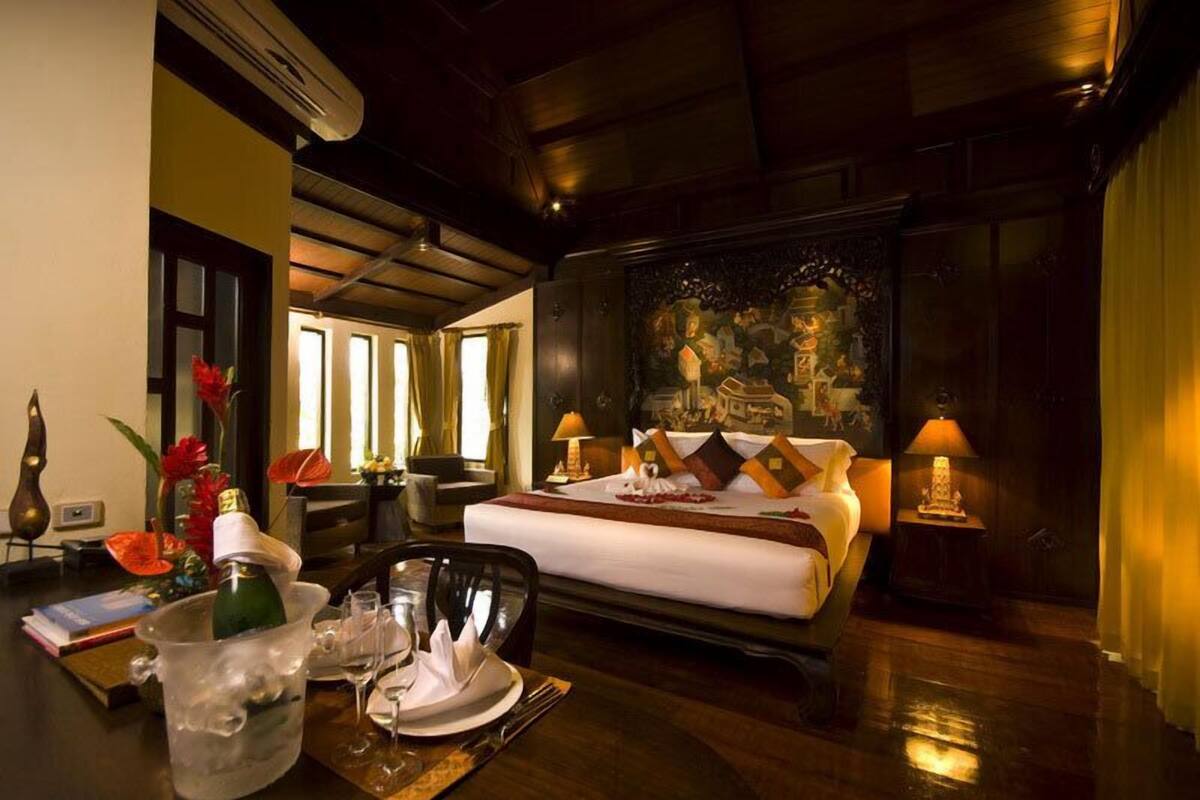 Une chambre d’hôtel avec un lit, des lampes de chevet, une table à manger avec une bouteille de champagne et un tableau au mur.