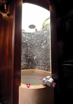 Un muro de piedra con un banco de piedra y una pequeña piscina con agua y pétalos de flores.