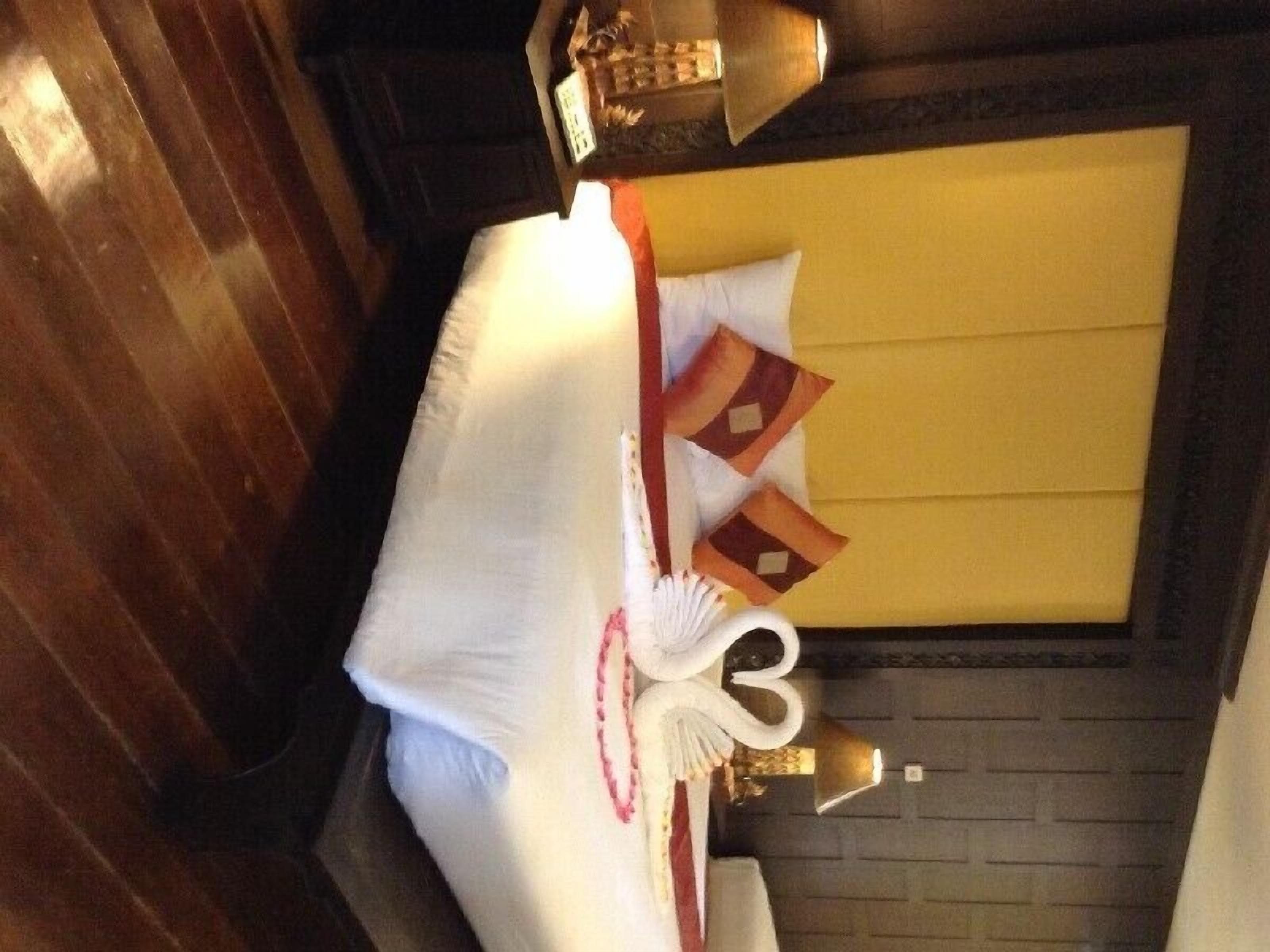 A neatly arranged bed with a white pillow, a decorative pillow with a red and brown pattern, and a white decorative item resembling a swan.