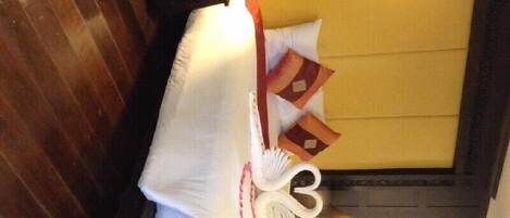 A neatly arranged bed with a white pillow, a decorative pillow with a red and brown pattern, and a white decorative item resembling a swan.