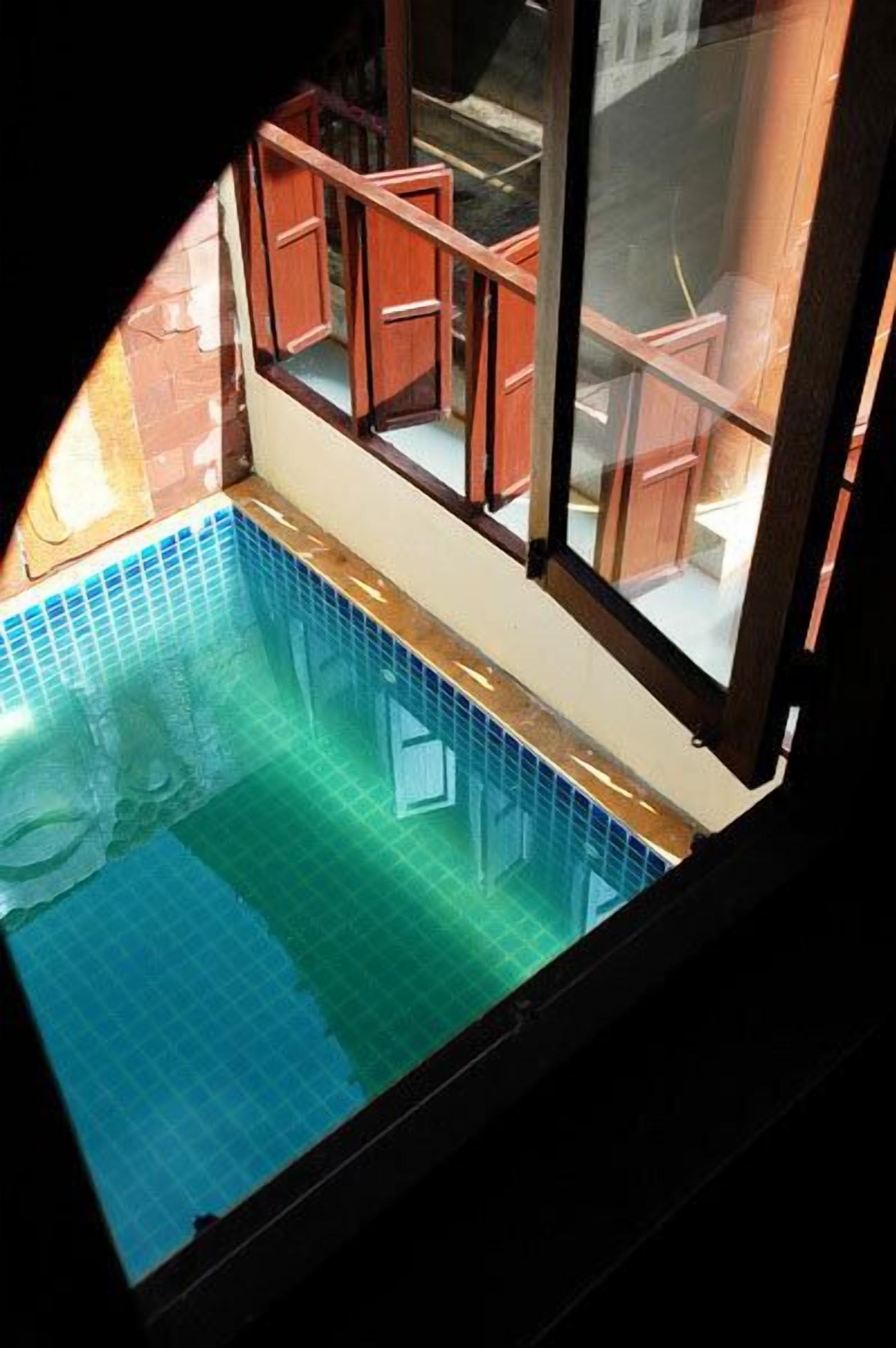 Blick auf ein Schwimmbecken mit Holzterrasse und Glasgeländer.