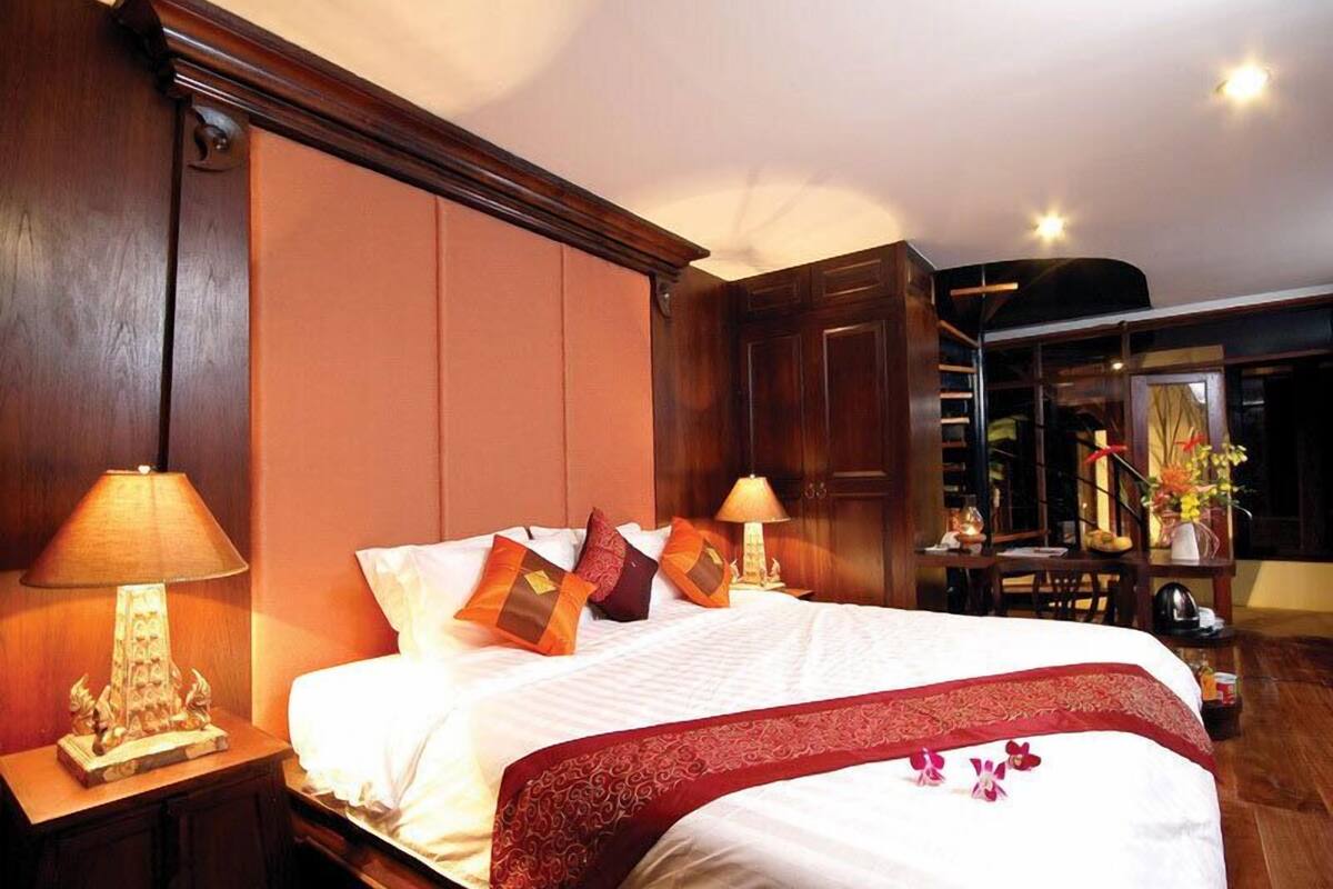 Une chambre d’hôtel avec un grand lit, une tête de lit en bois, deux lampes de chevet et un coussin décoratif rouge.