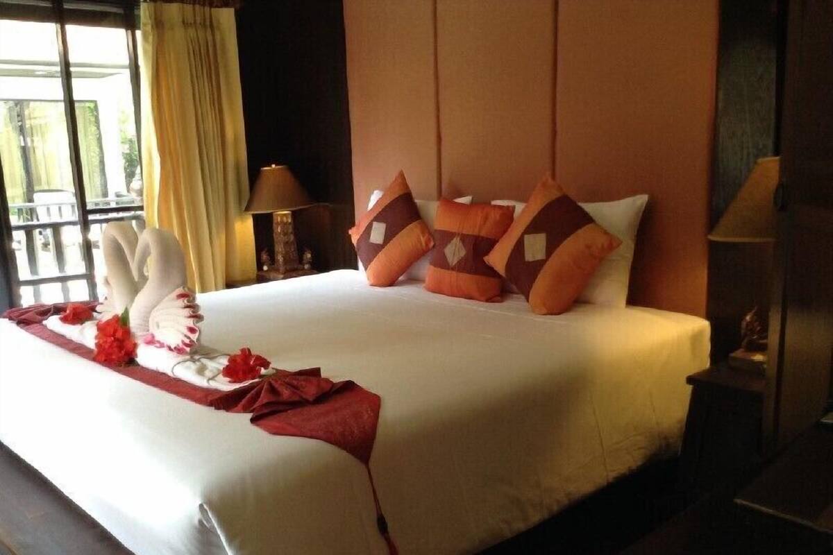 Une chambre d’hôtel avec un grand lit, une table de chevet, une lampe et une fenêtre avec des rideaux.