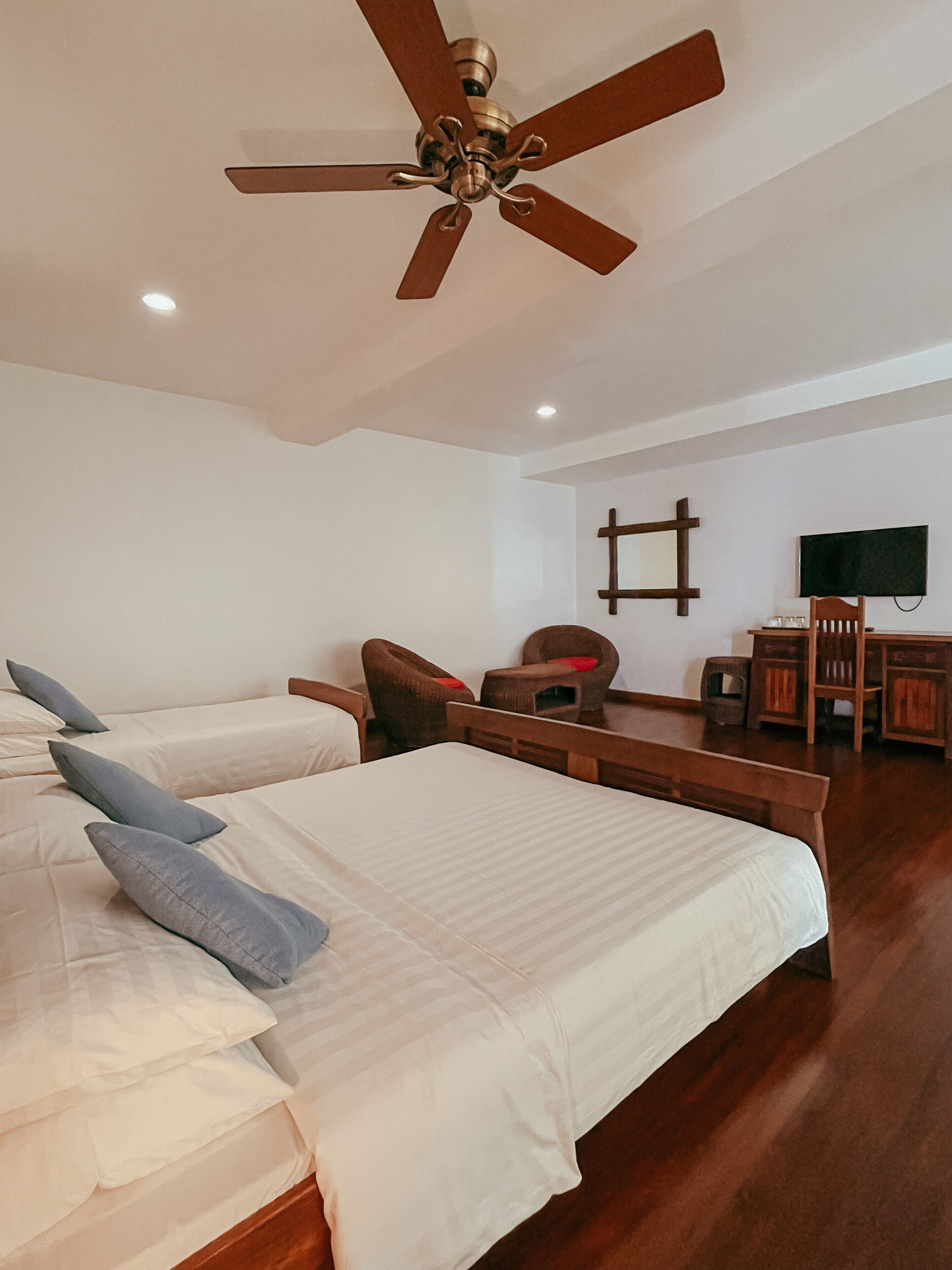 A bedroom with two beds, a wooden desk, a chair, a television, and a ceiling fan.