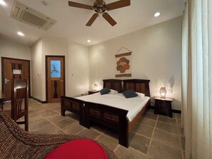 A bedroom with a large bed, a ceiling fan, a wall-mounted artwork, and a small table with a lamp. - Corto del Mar Hotel (Coron)
