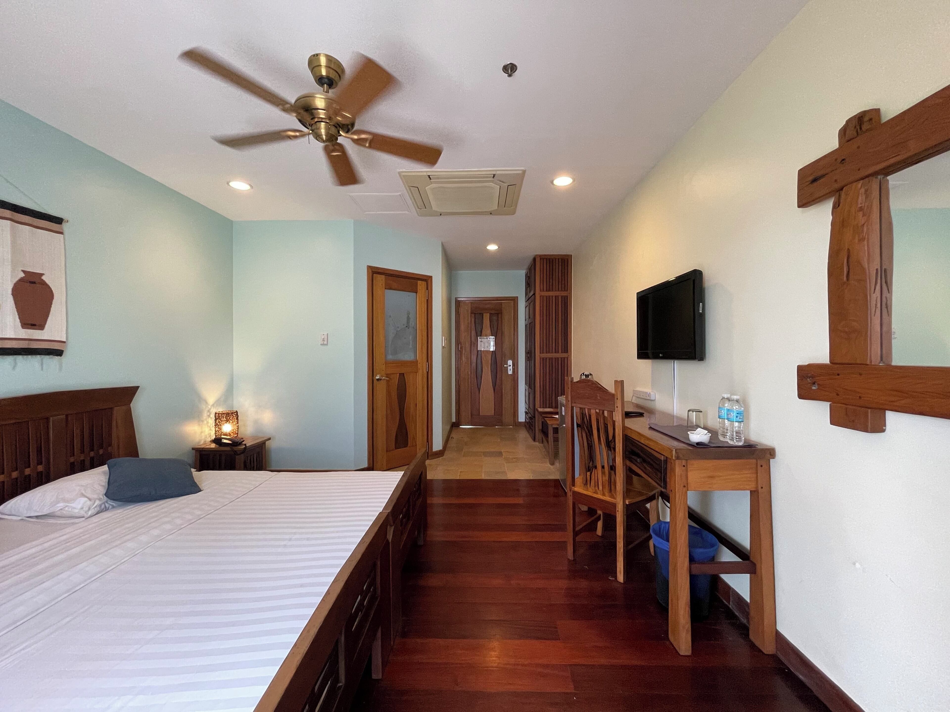 A hotel room with a bed, a desk, a television, and a ceiling fan.